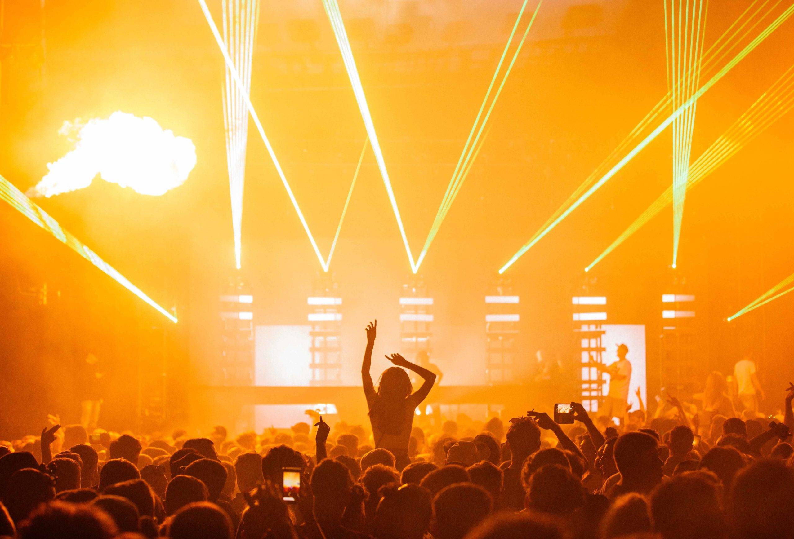 A beautiful shot of a live concert performance with a yellow light show and a big crowd cheering